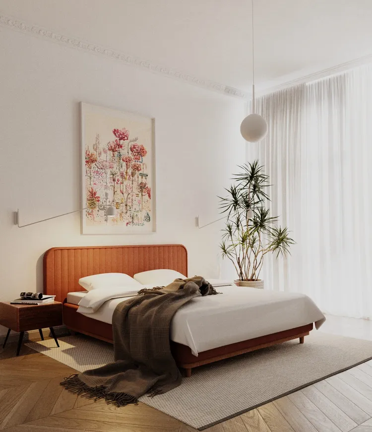 Jasna sypialnia z łóżkiem w kolorze rdzy, botaniczną grafiką, rośliną doniczkową, przezroczystymi zasłonami, jasną podłogą i delikatnym oświetleniem.